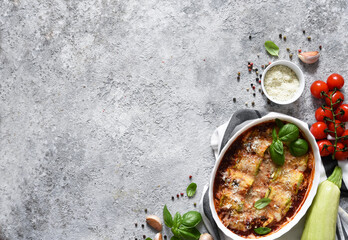 Baked zucchini rolls with ricotta cheese and tomato sauce and basil on a concrete table. View from above.