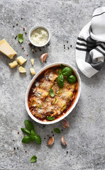 Baked zucchini rolls with ricotta cheese and tomato sauce and basil on a concrete table. View from above.