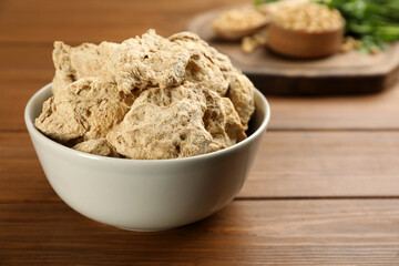 Dehydrated soy meat chunks in bowl on wooden table, closeup