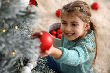 Cute little girl decorating Christmas tree at home, above view