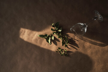 Dark brown background of craft paper with copy space with a small glass and leaves , low lighting, view from above