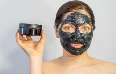 Emotional Woman with black charcoal face mask and a lotion of cream in her hands