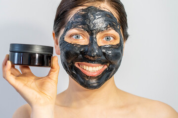 Emotional Woman with black charcoal face mask and a lotion of cream in her hands