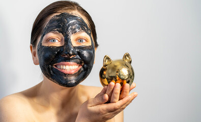 Emotional Woman with black charcoal face mask and with a piggy bank in her hands