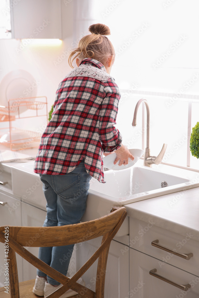 Poster Little girl washing dishes in kitchen at home, back view