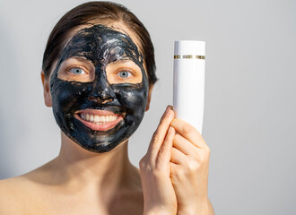Emotional Woman with black charcoal face mask and white tube of cream in her hands