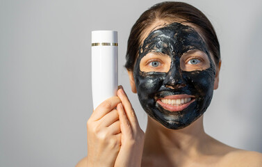 Emotional Woman with black charcoal face mask and white tube of cream in her hands
