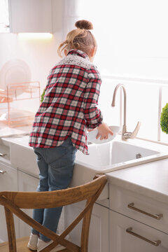 Little Girl Washing Dishes In Kitchen At Home, Back View