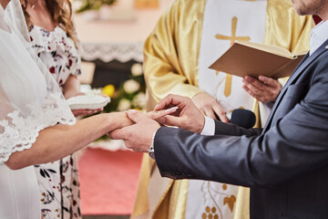 Obraz na płótnie Canvas Newlyweds exchange rings during a wedding in a Catholic church