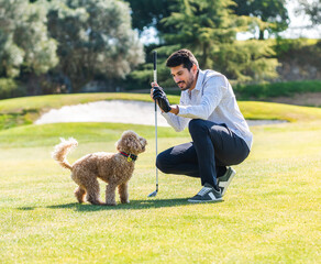 Young Caucasian male playing with his Goldendoodle dog on a professional golf course