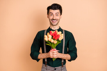 Photo of young handsome man happy positive smile hold flowers bouquet celebration isolated over beige color background