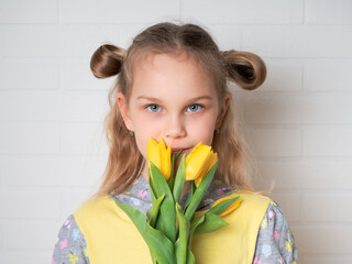 Beautiful young girl in a yellow blouse with tulips flowers in her hands on a light background