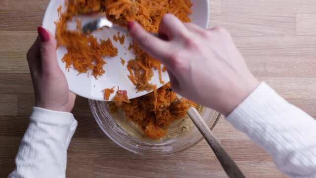 Hands Adding Grated Carrots with Tablespoon into Carrot Cake Dough. - Top Down Shot 