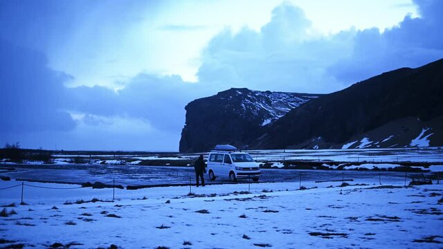 Tourist walking up to his campervan in a parking-lot with breathtaking landscape of Iceland in background.