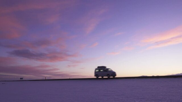 Panoramic landscape shot of Volkswagen campervan driving on highway in Iceland with purple sky while sunset.