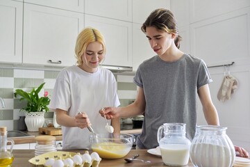 Teenagers guy and girl cooking pancakes in kitchen together