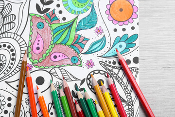Antistress coloring page and pencils on light wooden table, flat lay