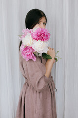 Stylish woman in linen dress holding peony bouquet at white fabric. Slow life. Aesthetic moment
