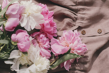 Beautiful peonies on rustic linen dress in soft sunny light in room, top view. Aesthetics. Slow life