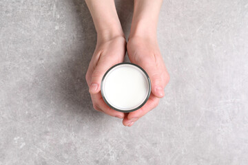 Woman holding glass of milk at light grey table, top view