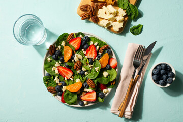 Summer salad with berries, cheese and spinach on blue background