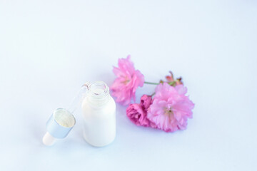 White serum bottle and pink cherry blossom. Natural organic skincare cosmetics concept. Selective focus