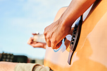 detail of hand playing an acoustic guitar on a sunny day with blue skies
