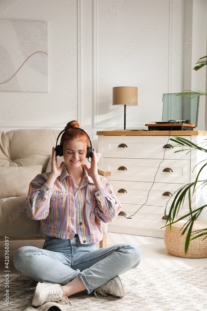 Poster Young woman listening to music with turntable in living room