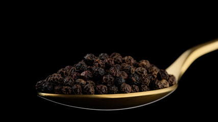 black pepper in golden spoon isolated on black background. Flavorful and aromatic peppercorn