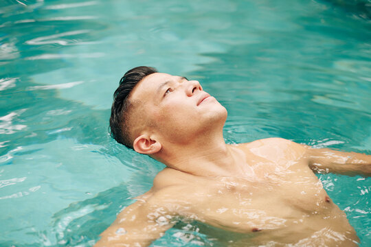 Fit Man Floating On Back In Swimming Pool And Looking At Sky