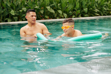 Father teaching his son swimming, he is controlling boy swimming with foam noodle