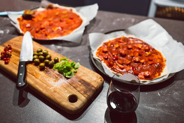 homemade vegan pizzas getting prepared on kitchen benchtop with glasses of wine next to them, healthy plant-based food