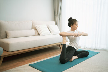 Portrait of gorgeous young asian woman practicing yoga at home stretching out while following a yoga routine.