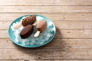 Chocolate popsicles and crushed ice on blue plate on wooden table. Copy space