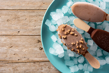 Chocolate popsicles and crushed ice on blue plate on wooden table.Top view. Copy space