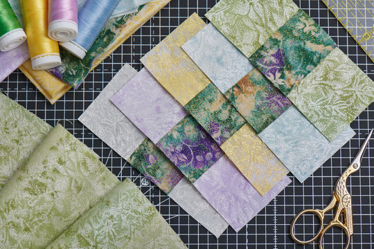Sewn square pieces of fabric, sewing and quilting accessories lying on a cutting mat