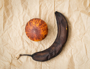 Rotten banana and spoiled tangerine on brown crumpled paper.