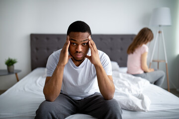 Sex or relationship difficulties. Unhappy black guy sitting on bed, massaging temples, overwhelmed...