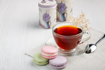 Multicolored macaroons and a cup of tea on a light wood kitchen table. Morning tea and sweets.