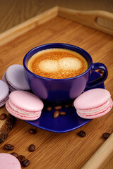 Cup of coffee, macaroons, and coffee beans on a platter on a wooden tray