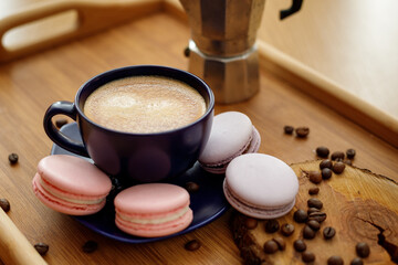 Cup of coffee, macaroons, and coffee beans on a platter and geyser coffee maker on a wooden tray