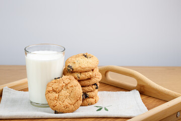A glass of milk and cookies with raisins on a wooden tray