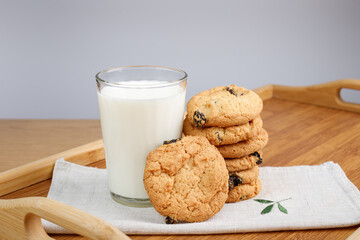 A glass of milk and cookies with raisins on a wooden tray