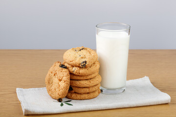 A glass of milk and cookies with raisins on the table.