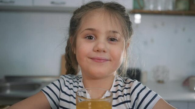Little girl drinks juice. Organic fruit drink. Girl with glass of orange juice. Organic healthy juice. Little girl at home with drink. Child drinks juice. Organic healthy products concept.