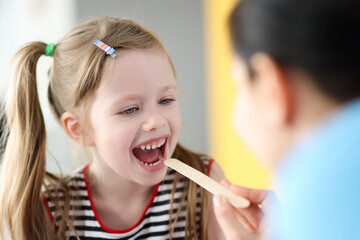 Pediatrician doctor examining throat of little girl with spatula