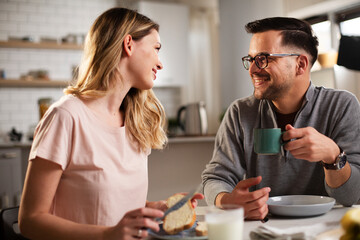 Beautiful young woman enjoying in breakfast with boyfriend. Happy young couple drinking coffee and eating sandwich at home..