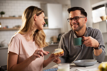 Fototapeta na wymiar Beautiful young woman enjoying in breakfast with boyfriend. Happy young couple drinking coffee and eating sandwich at home..