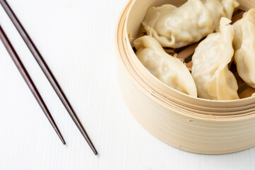 Top view of steamer with gyozas and chopsticks, on white wood, horizontal, with copy space