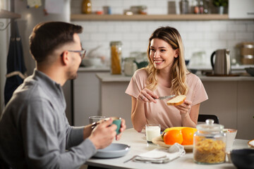 Beautiful young woman enjoying in breakfast with boyfriend. Happy young couple drinking coffee and eating sandwich at home..